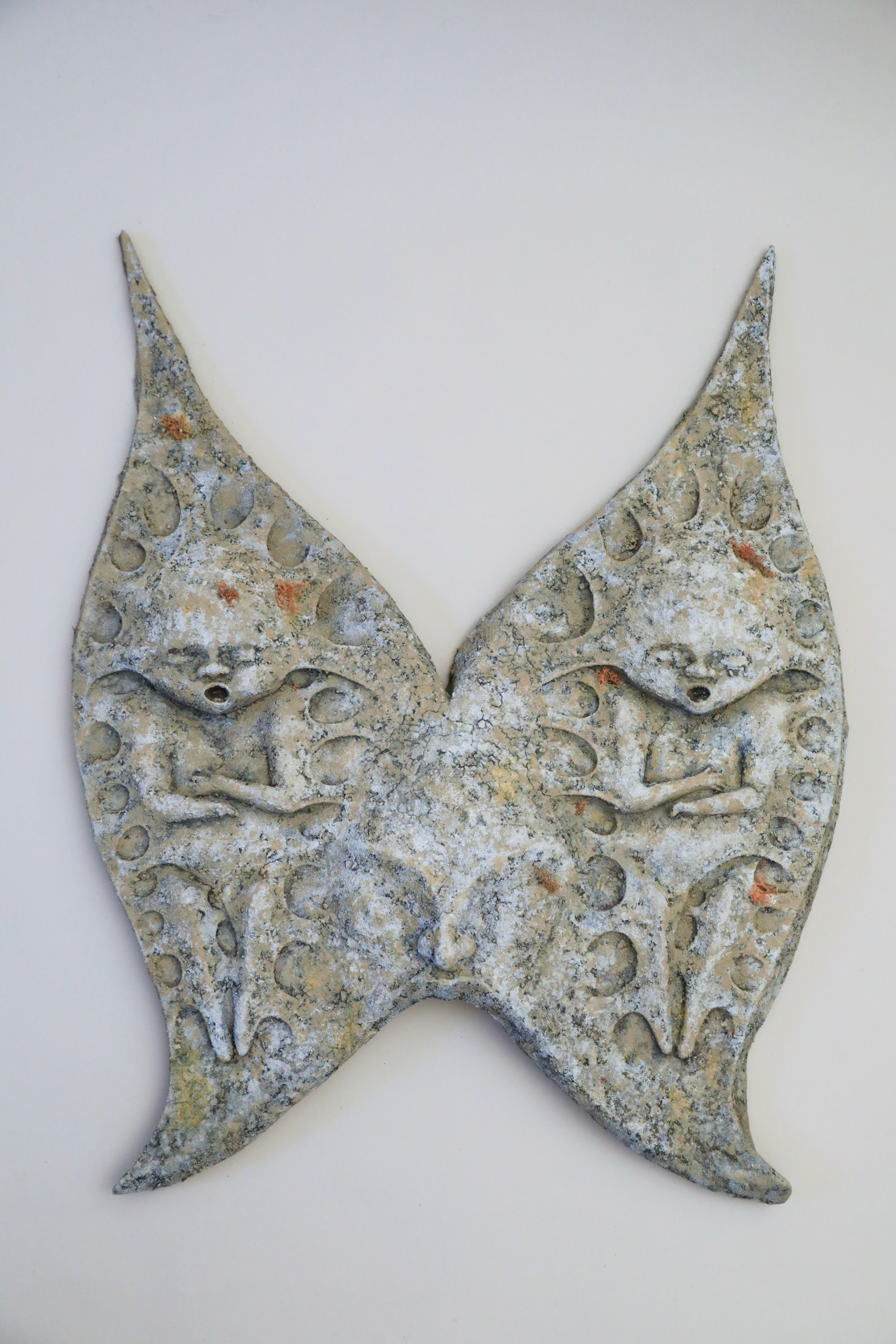 Latex stone headpiece shaped like two winged forms joined at the center, each containing a small sculpted baby figure in relief. The piece covers the wearer’s head and face, merging organic and mechanical forms.